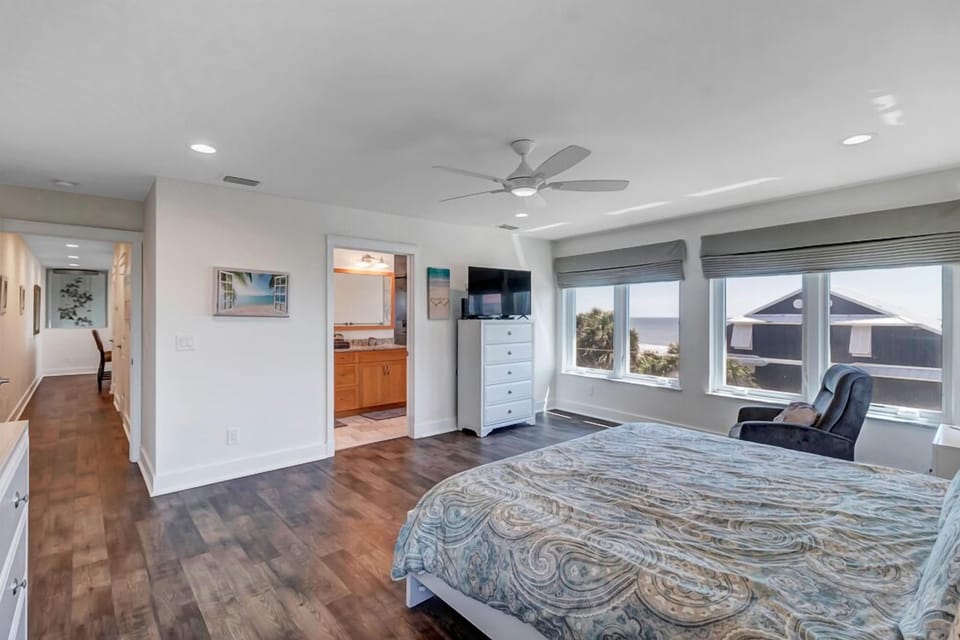 - Spacious bedroom with ocean facing windows, smart TV, and white dresser setup
- Room connects to a private ensuite and hallway for added accessibility and ease
- Relax in the reading chair or enjoy sunrise light from bed each morning