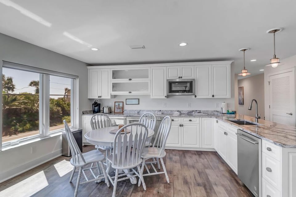 - White cabinetry and granite countertops frame this bright, functional kitchen
- Round dining table offers seating beside large windows with garden views
- Stainless steel dishwasher and microwave complete the modern essentials