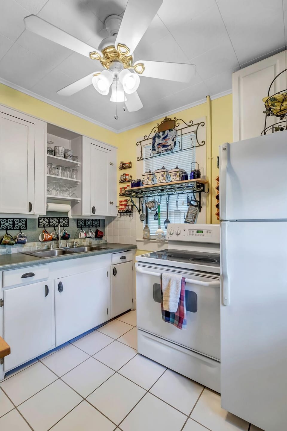 - Make home cooked meals with ease in this cheerful space with stove, fridge, and open shelving
- Vibrant mugs, plates, and personal touches add warmth to every meal
- Fully stocked kitchen with plenty of character and convenience