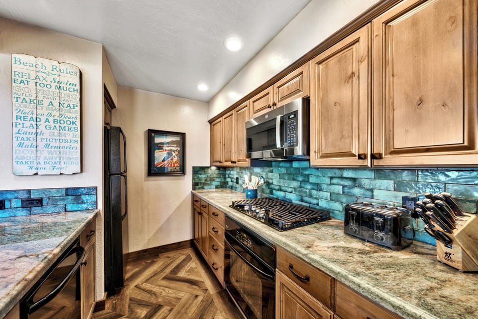 Your fully equipped galley kitchen features warm wood cabinets, stunning blue tile backsplash, and granite counters perfect for preparing vacation meals.