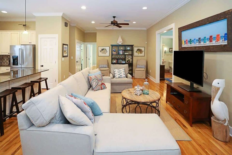 - Living room with a cozy sectional, perfect for relaxing after a day of adventure - Features a flat screen TV & coastal themed decor, creating a calming atmosphere - Open concept design with easy access to the kitchen & other areas of the home