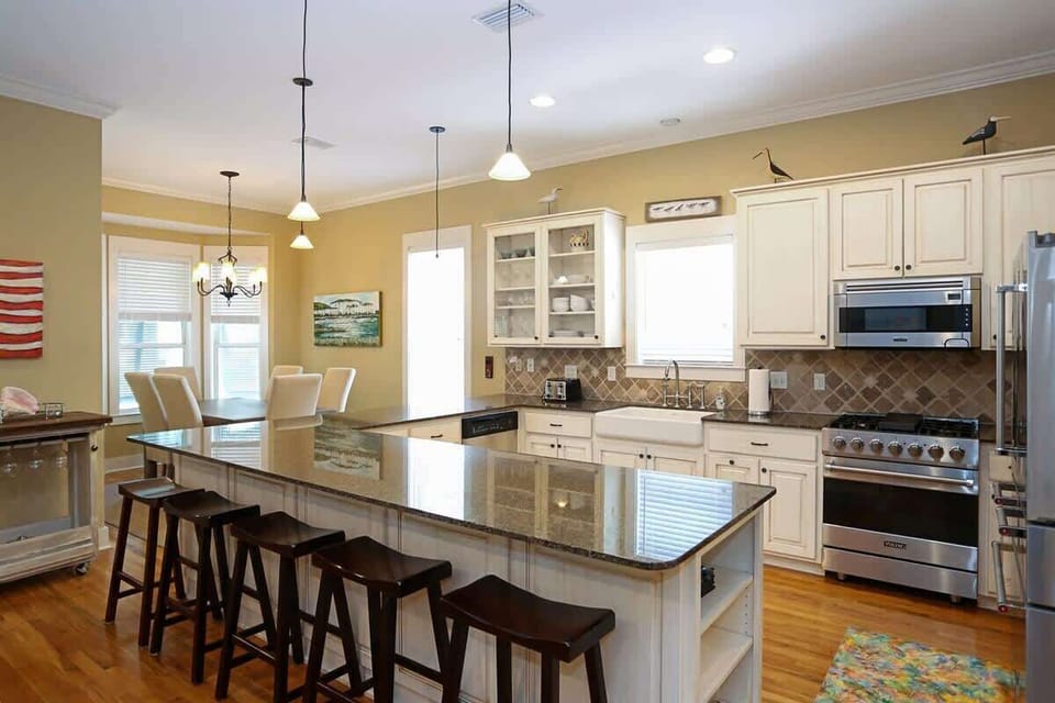- Kitchen featuring a large island with barstool seating, perfect for casual dining - Modern appliances, including a farmhouse sink, gas range, & stainless steel fridge - Beautiful natural wood floors & decorative touches like pendant lighting & artw