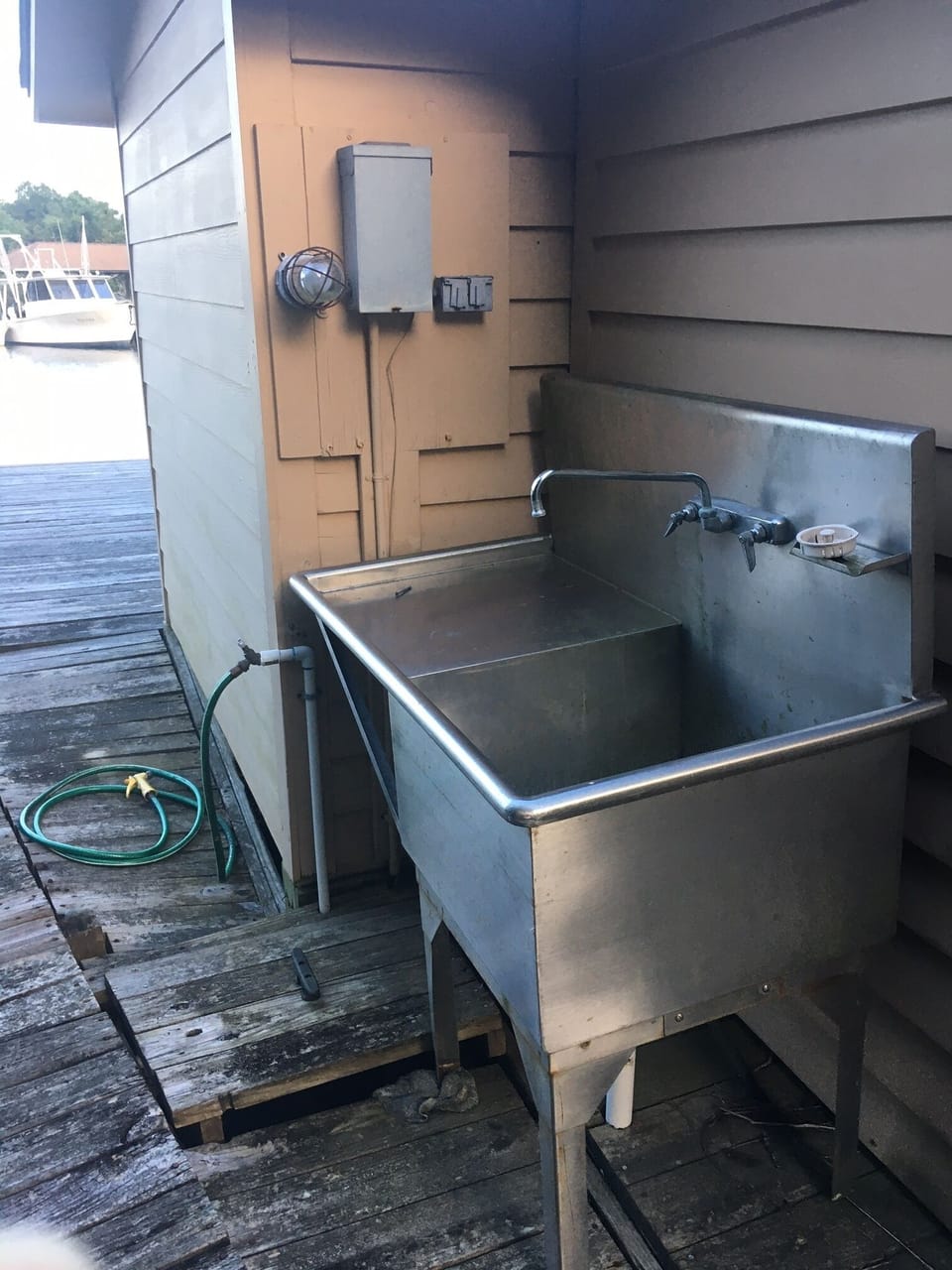 Fish cleaning sink with a wall mounted light and a hose for rinsing things off.