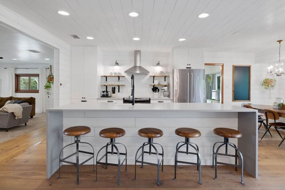 Bright farmhouse kitchen with open shelving and river‑view dining table—cook together, then step right out to the treetop deck.