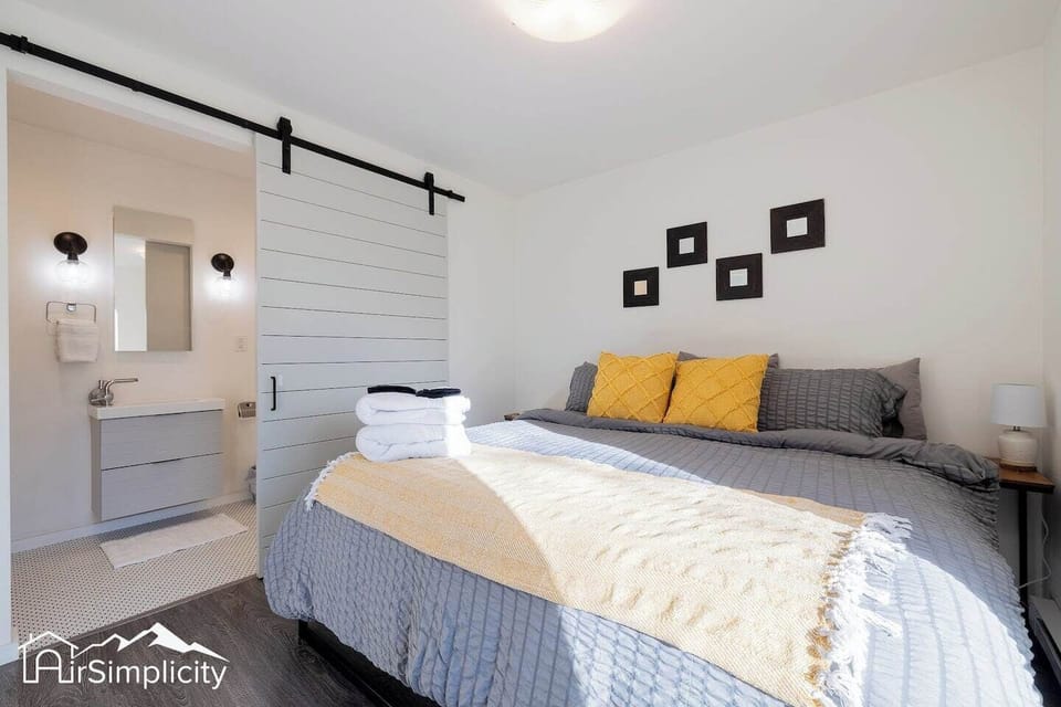 - Bright and inviting bedroom with a king sized bed dressed in cozy gray and gold tones
- Modern barn door opens to a sleek ensuite bathroom with stylish lighting
- Towels and essentials thoughtfully prepared for a comfortable, restful stay