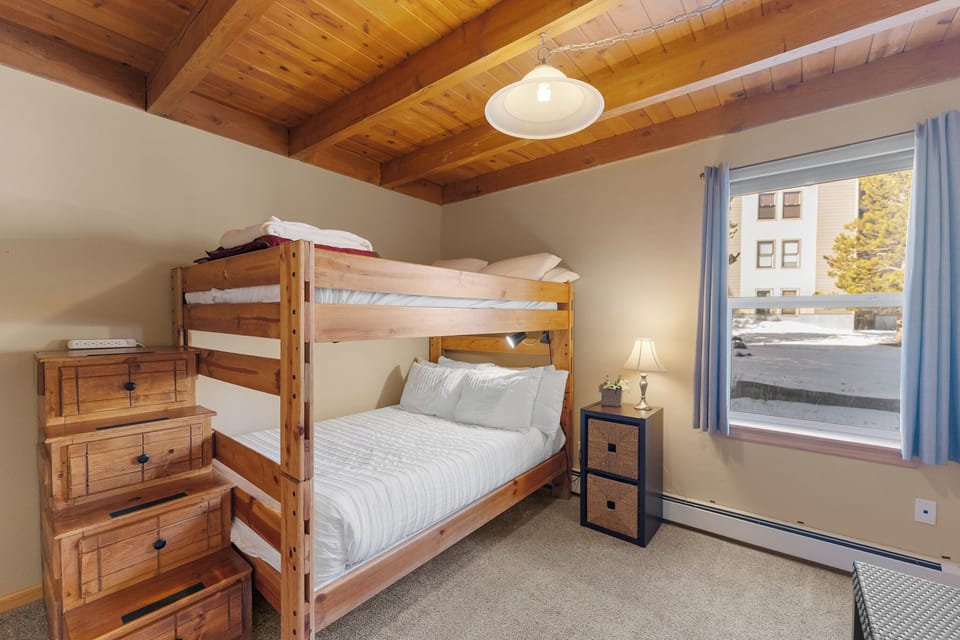 Rest in your cozy bunk bed beneath exposed wooden beams, where warm lighting creates the perfect mountain cabin atmosphere.