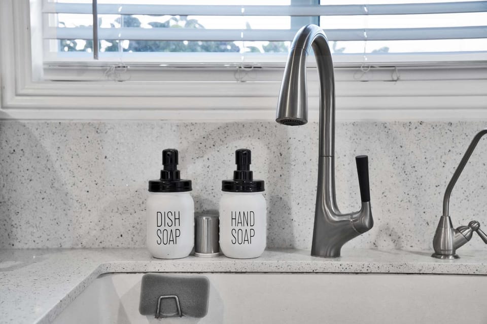 Bright kitchen sink area with a modern faucet, dish and hand soap dispensers, and a window offering a pleasant view.