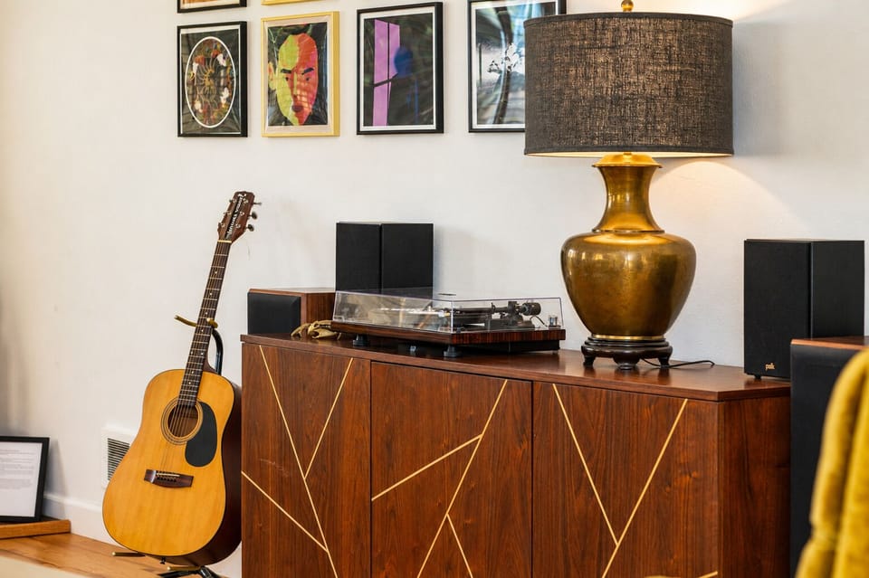 Relax in your stylish living space featuring vintage vinyl setup, acoustic guitar, and curated artwork—perfect for music lovers