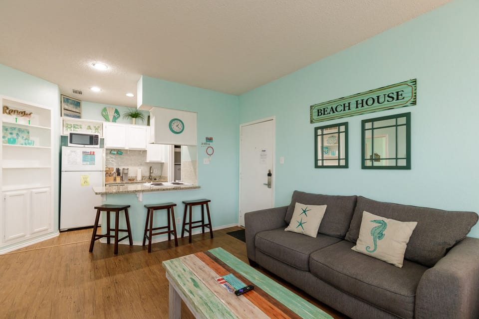 Relax in your coastal-themed living space with comfy seating, beach-inspired decor, and an open kitchen perfect for preparing meals.