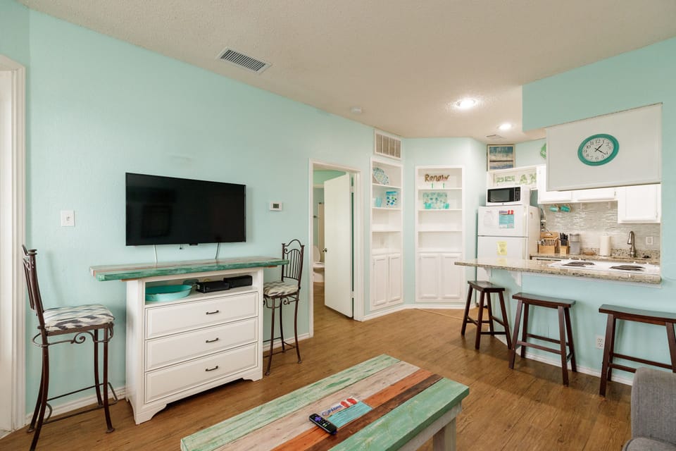 Unwind in your bright coastal living space with soothing mint walls, modern kitchen, and comfortable seating for relaxing after beach adventures.
