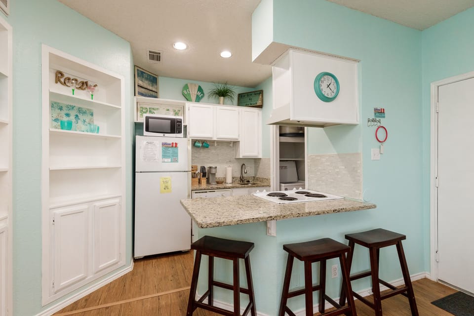 Your bright beachside kitchen invites morning coffee prep with granite counters, modern appliances, and cheerful coastal colors creating the perfect vacation vibe.