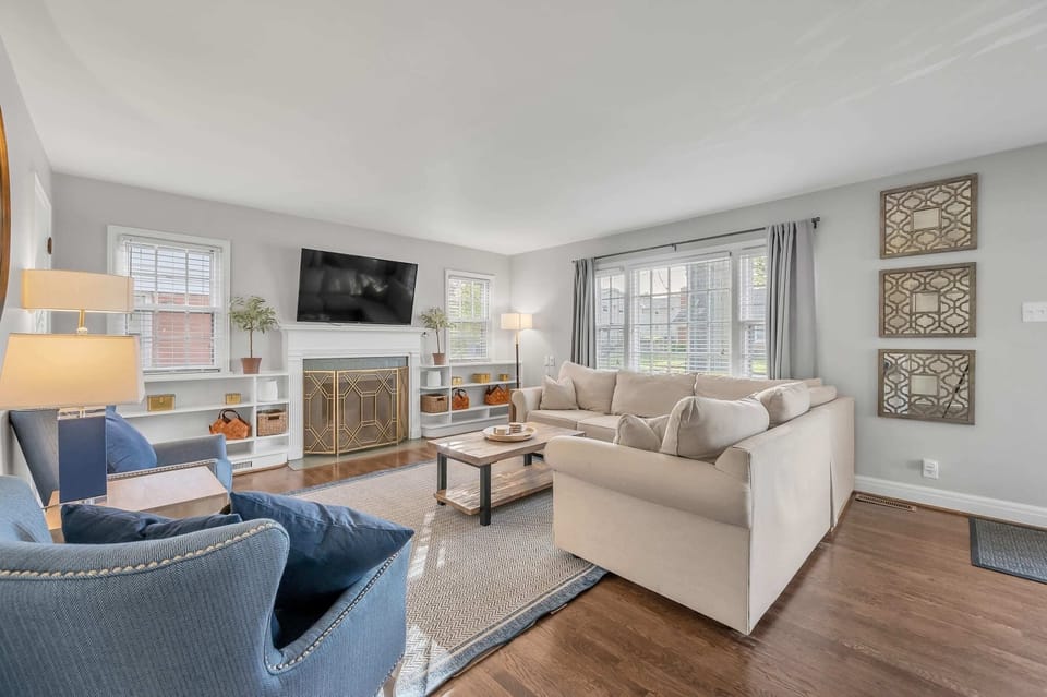Spacious and stylish living room in our Airbnb with seating for 10 and a large, wall-mounted smart TV. Modern decor, neutral color palette, and ample natural light create a calming atmosphere. Perfect for relaxing after a day of exploring and spending time with loved ones.