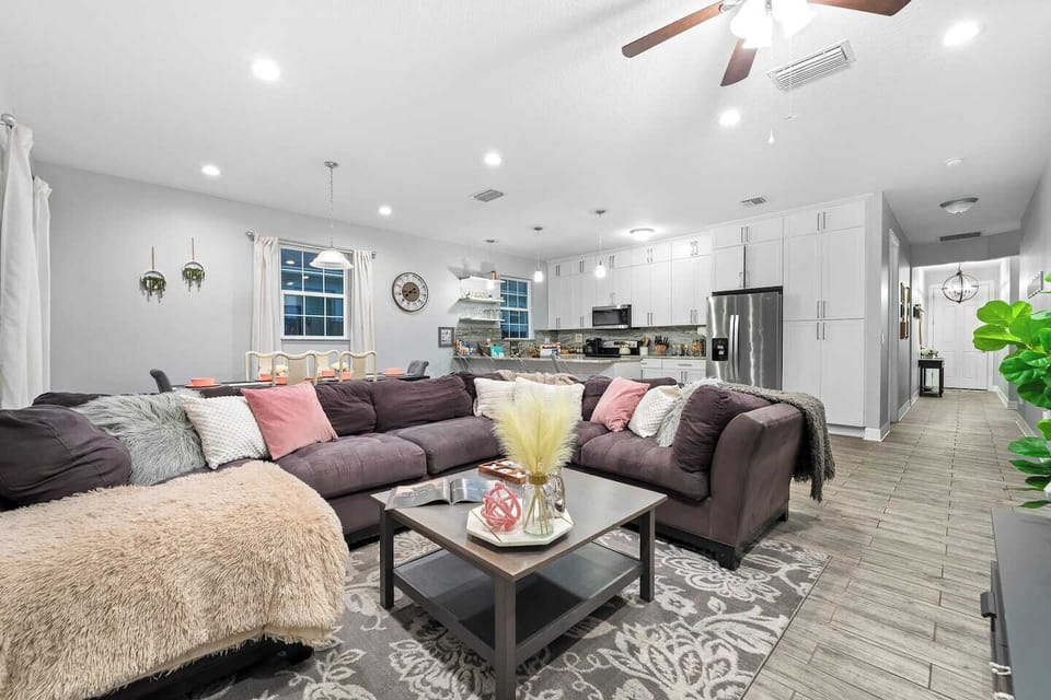 Living room with a large sectional couch and a 55" smart TV. The sliding glass door leads out to the fenced-in backyard and back patio area, where the outdoor sectional and hot tub are located.
