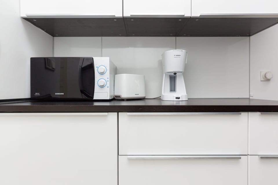 A close-up of a kitchen area with neatly arranged appliances, including a microwave and a kettle, on white countertops.