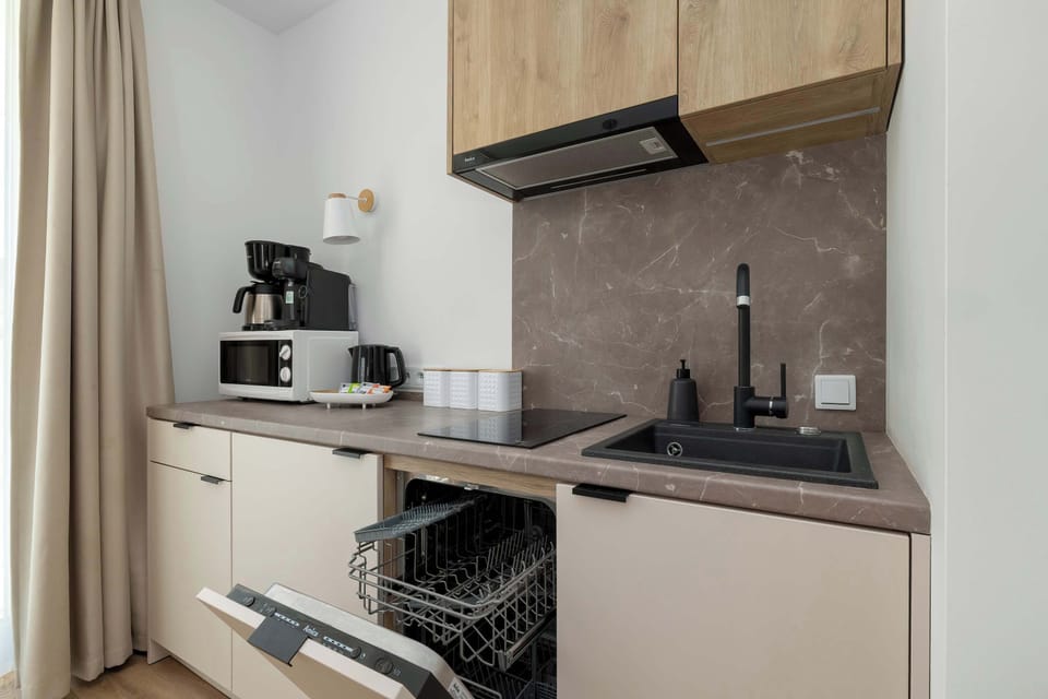 A kitchen scene highlights lower cabinets and an open oven beneath the countertop. Dark accents contrast with light wood surfaces.