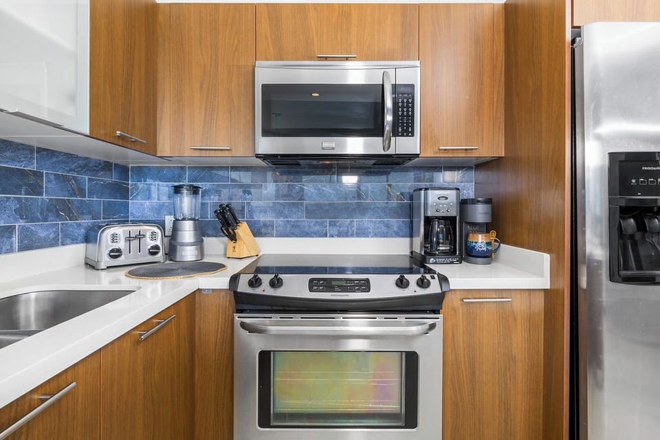A modern, fully-equipped kitchen with stainless appliances, stylish blue tile backsplash, and wood cabinetry awaits your culinary adventures.