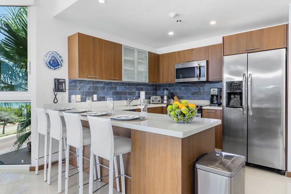 Your fully equipped kitchen invites you to prepare fresh meals with modern appliances, sleek countertops, and a breakfast bar perfect for casual dining with tropical views.