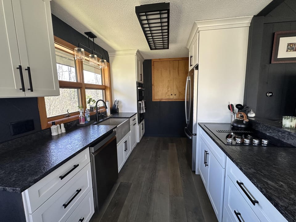 Renovated kitchen with black granite counters, white cabinetry, concrete farmhouse sink, and stainless steel appliances.