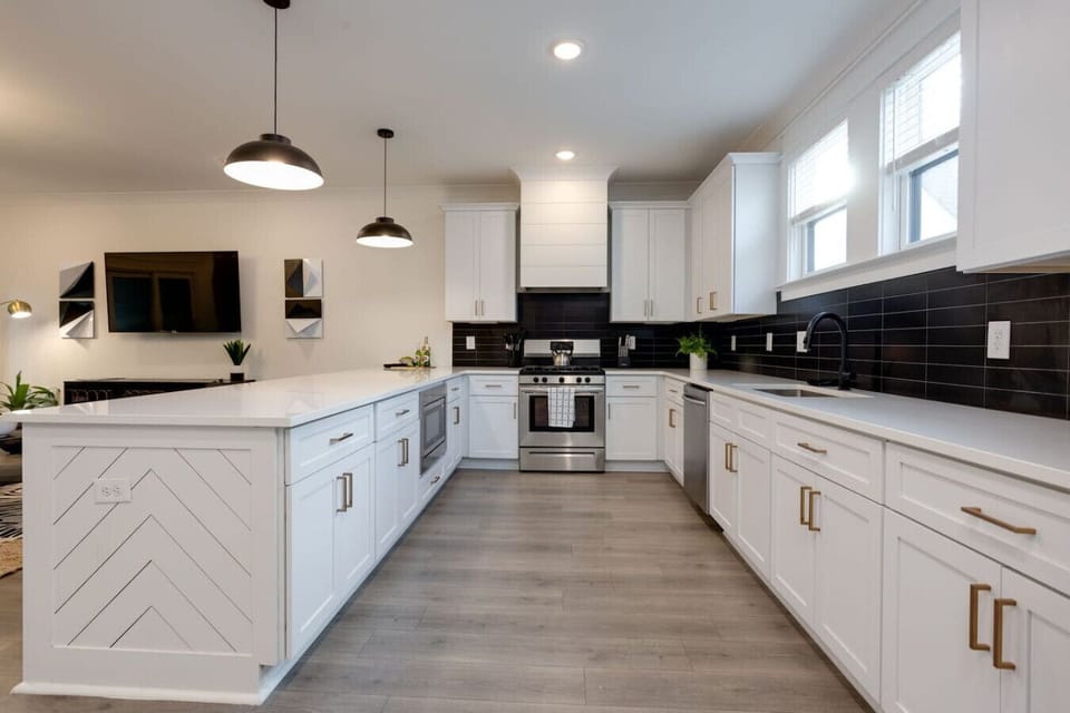Kitchen with dark cabinetry, marble island with bar stools, pendant lights, and stainless appliances