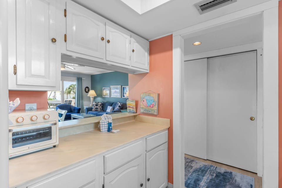 Step into your bright kitchen where coral walls and white cabinets create a cheerful cooking space, complete with modern appliances and an open view to your cozy living area.