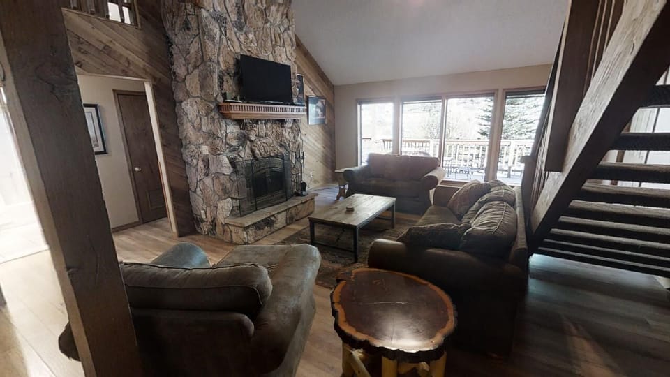 Settle in and feel right at home in this spacious living area, where a stunning stone fireplace anchors cozy seating and natural light floods through oversized windows revealing snowy mountain views beyond your deck.