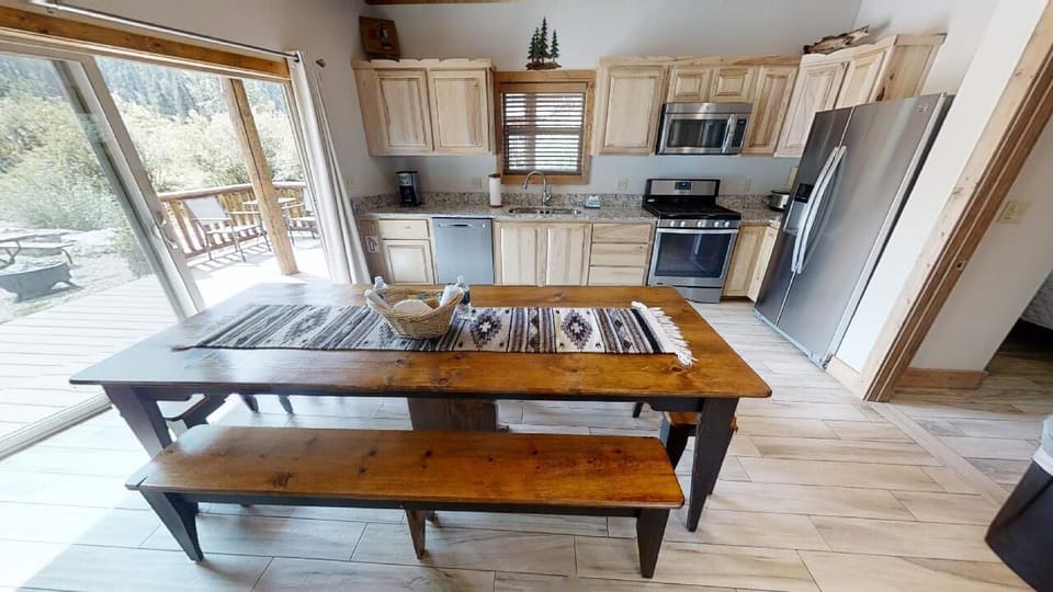 Your mountain retreat kitchen features warm wood cabinetry, modern stainless appliances, and a rustic dining table where you can gather for home-cooked meals with forest views just beyond the deck.