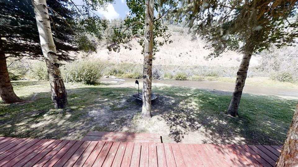 A peaceful riverfront setting with mature birch trees and natural landscape surrounding the property. A wooden deck offers direct access to the serene outdoor space.