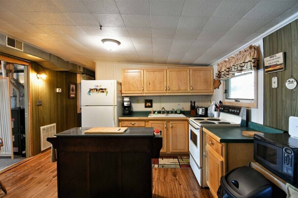 The kitchen of the Bony Lake North vacation home, featuring light wood cabinets, green countertops, a white refrigerator, and a dark kitchen island with a wooden cutting board.