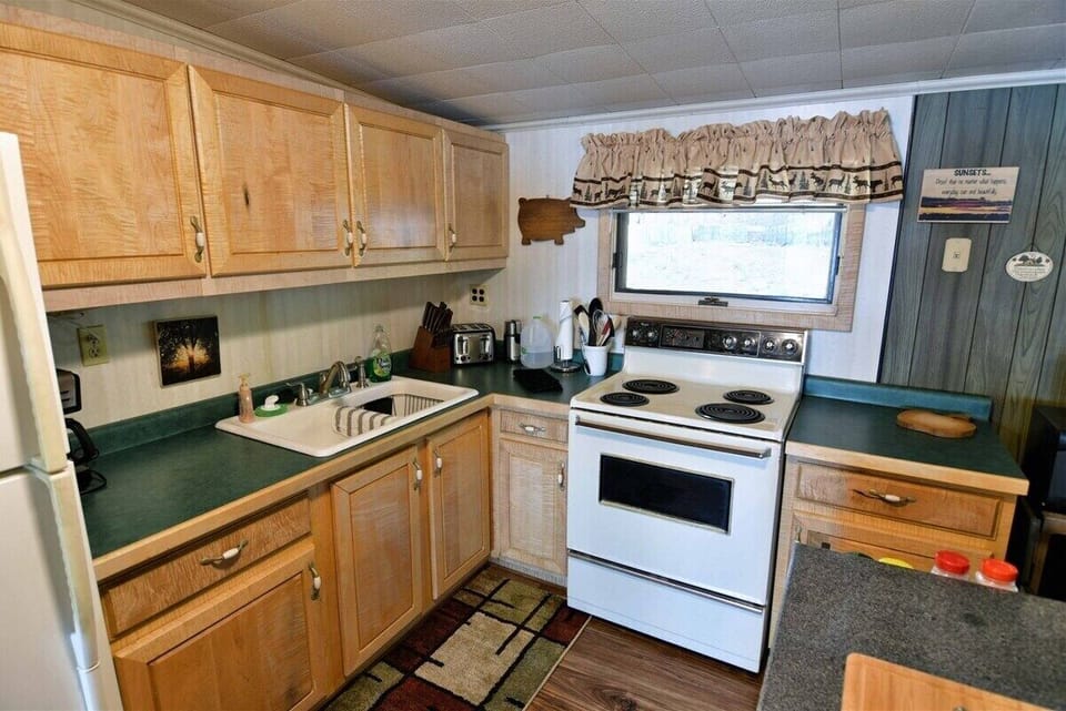 The kitchen of the Bony Lake North vacation home, featuring light wood cabinets, green countertops, a white refrigerator, and a dark kitchen island with a wooden cutting board.
