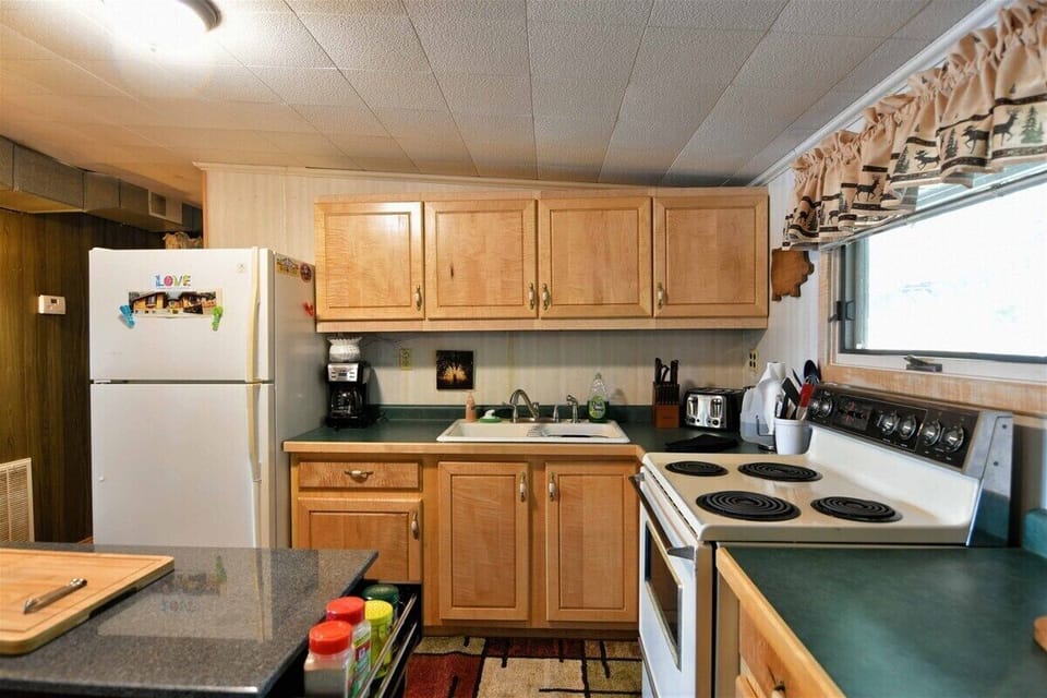 The kitchen of the Bony Lake North vacation home, featuring light wood cabinets, green countertops, a white refrigerator, and a dark kitchen island with a wooden cutting board.