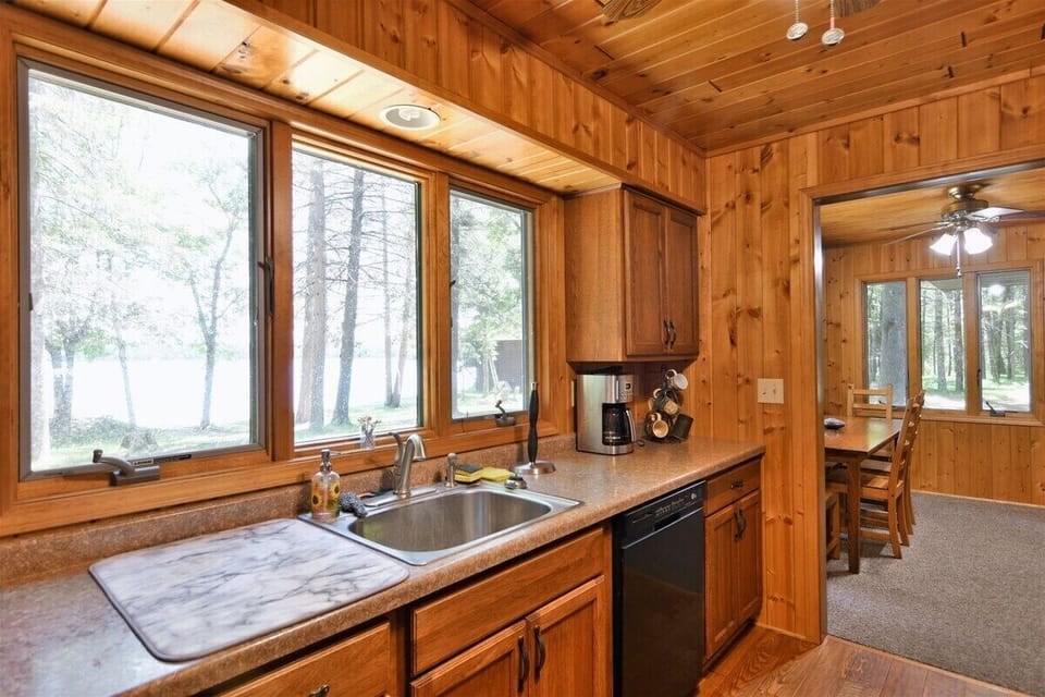 A galley-style kitchen with pine-paneled walls and ceiling, featuring a stainless steel sink set into a laminate countertop.