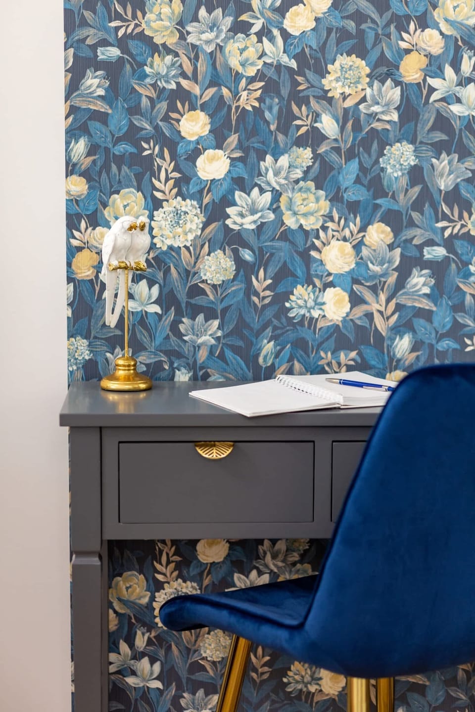 A bedroom corner featuring a floral wallpaper accent and a modern navy blue chair.

