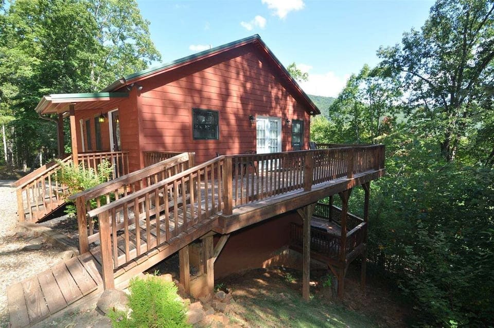 The elevated wraparound deck extends alongside the cabin with railings overlooking the forest. Outdoor living space provides wooded views in Bryson City.