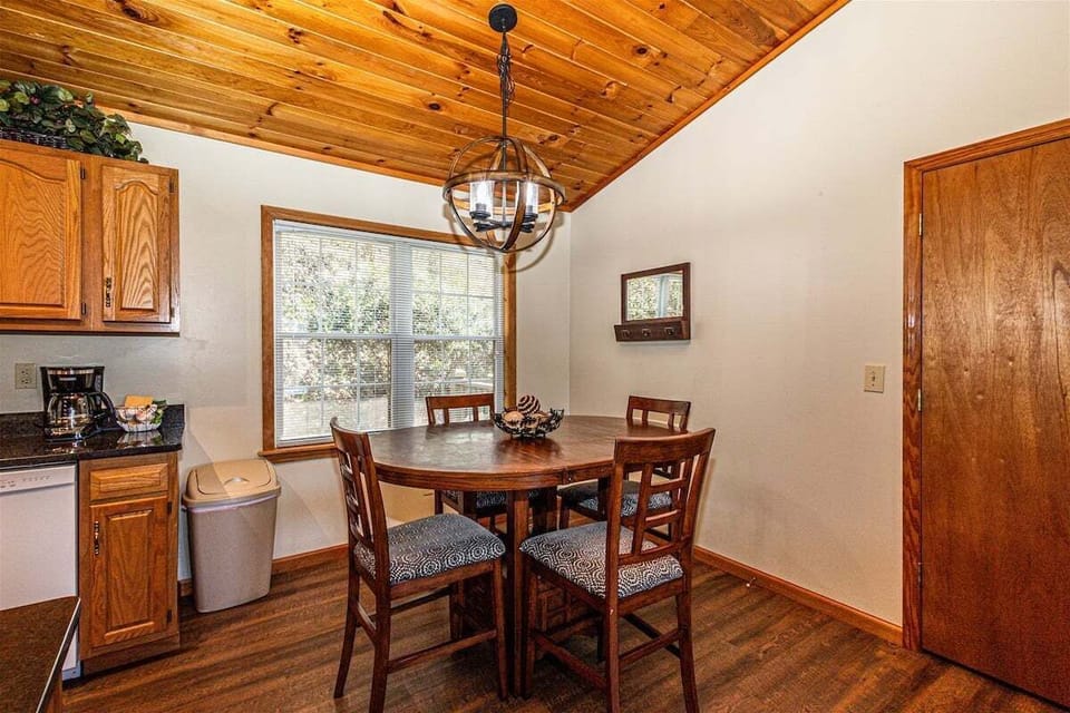 Dining area with a wooden table and chairs beneath a hanging light fixture, surrounded by wood-paneled walls and ceiling. Located at Big Oaks near Bryson City, NC, offering easy access to Great Smoky Mountains attractions.