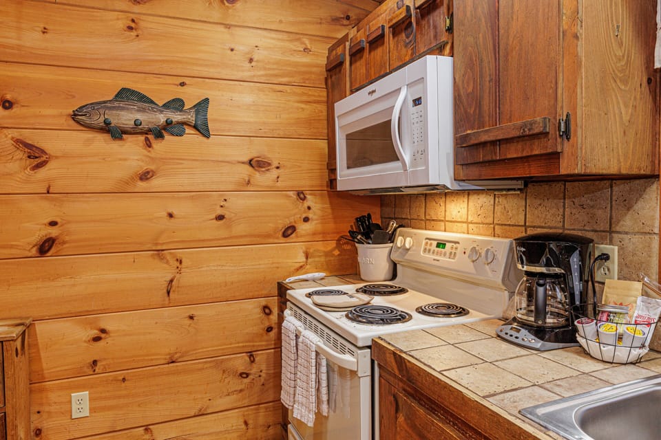 A compact kitchen includes tiled countertops, a coffee maker, microwave, and electric range. The wood interior creates a cozy cabin atmosphere.