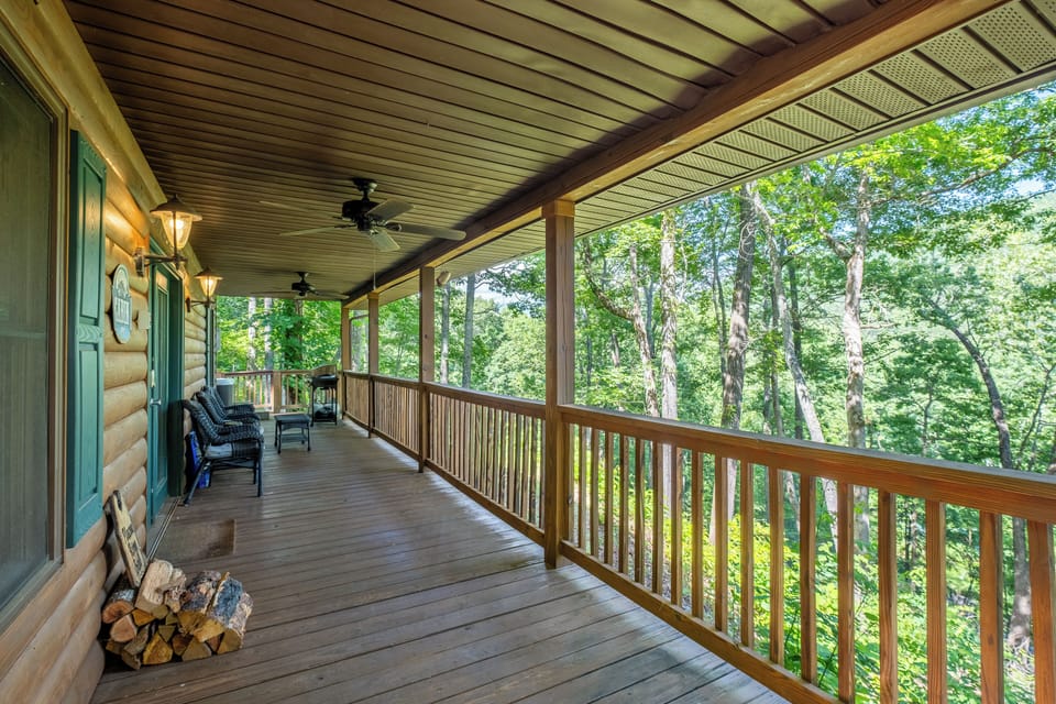 A long-covered deck with rocking chairs overlooks the surrounding forest. The spacious porch provides shaded outdoor seating at the Bryson City cabin.