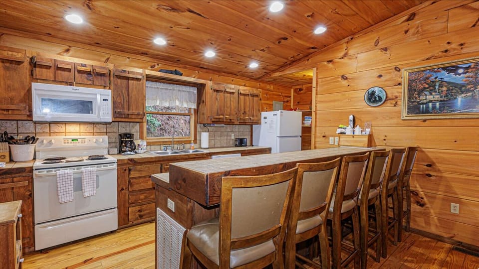 The open kitchen features wood cabinetry, a center island with bar seating, and full-size appliances. This inviting space is designed for preparing meals during your Bryson City stay.