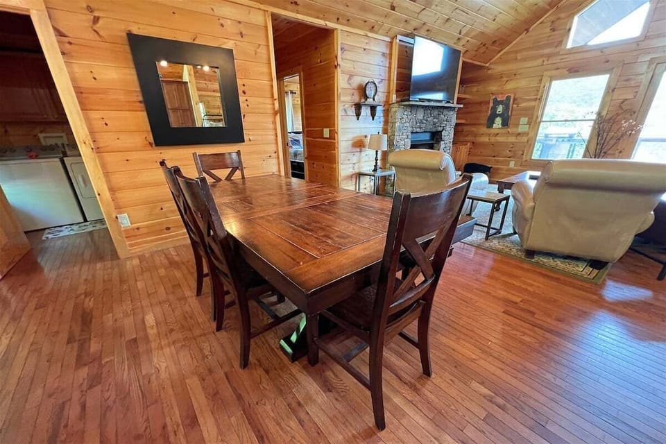 The open-concept dining area flows into the great room at Smoky Mountain High, featuring warm wood finishes and a stone fireplace.