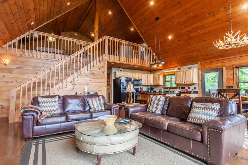 Open living room at A Walk in the Clouds featuring leather seating, loft staircase, and high ceilings in Bryson City. Located near Great Smoky Mountains National Park with spacious interior layout.