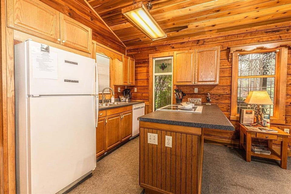 Full kitchen with wood cabinetry, refrigerator, and island countertop providing meal preparation space. Functional cabin kitchen located near Great Smoky Mountains attractions.