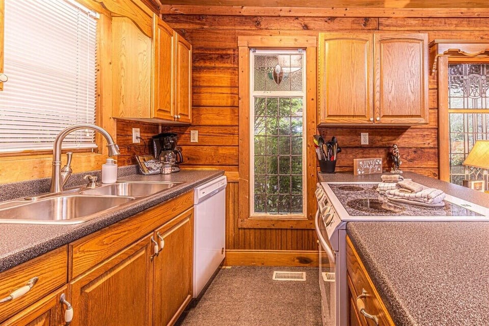 Galley-style kitchen with wood cabinets, laminate countertops, double sink, and exterior door access. Functional cabin kitchen space at Creekside Hideaway in Bryson City, NC.