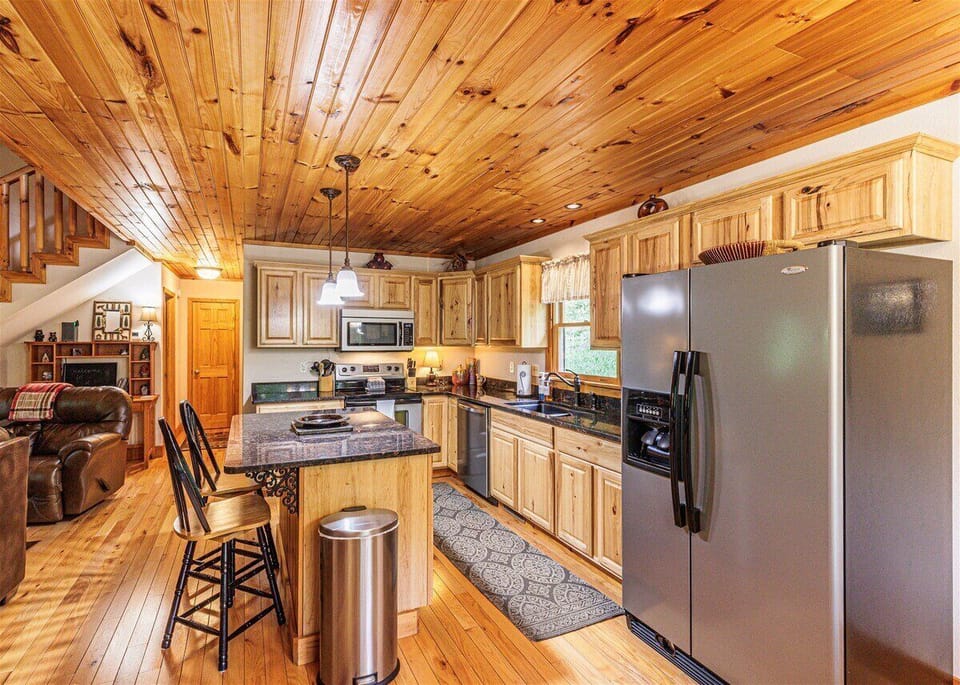 Kitchen with natural wood cabinetry, stainless steel refrigerator, center island, and bar seating. Convenient space for preparing meals during a Bryson City cabin stay.