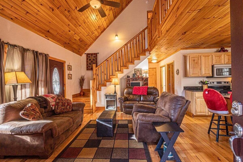 Open-concept great room featuring leather seating, area rug, staircase to loft, and kitchen beyond. The spacious interior offers comfortable gathering space near downtown Bryson City.