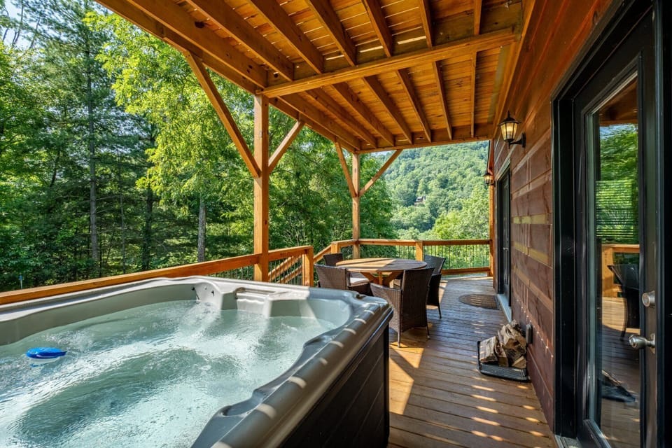 Covered lower deck with private hot tub and outdoor seating overlooking wooded mountain scenery in Bryson City, NC near Nantahala Outdoor Center and Smoky Mountain attractions.