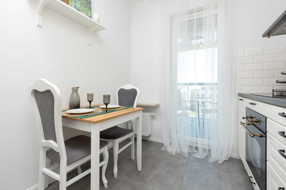 A dining nook with a small table, green table settings, and a white curtain allowing natural light to stream in.