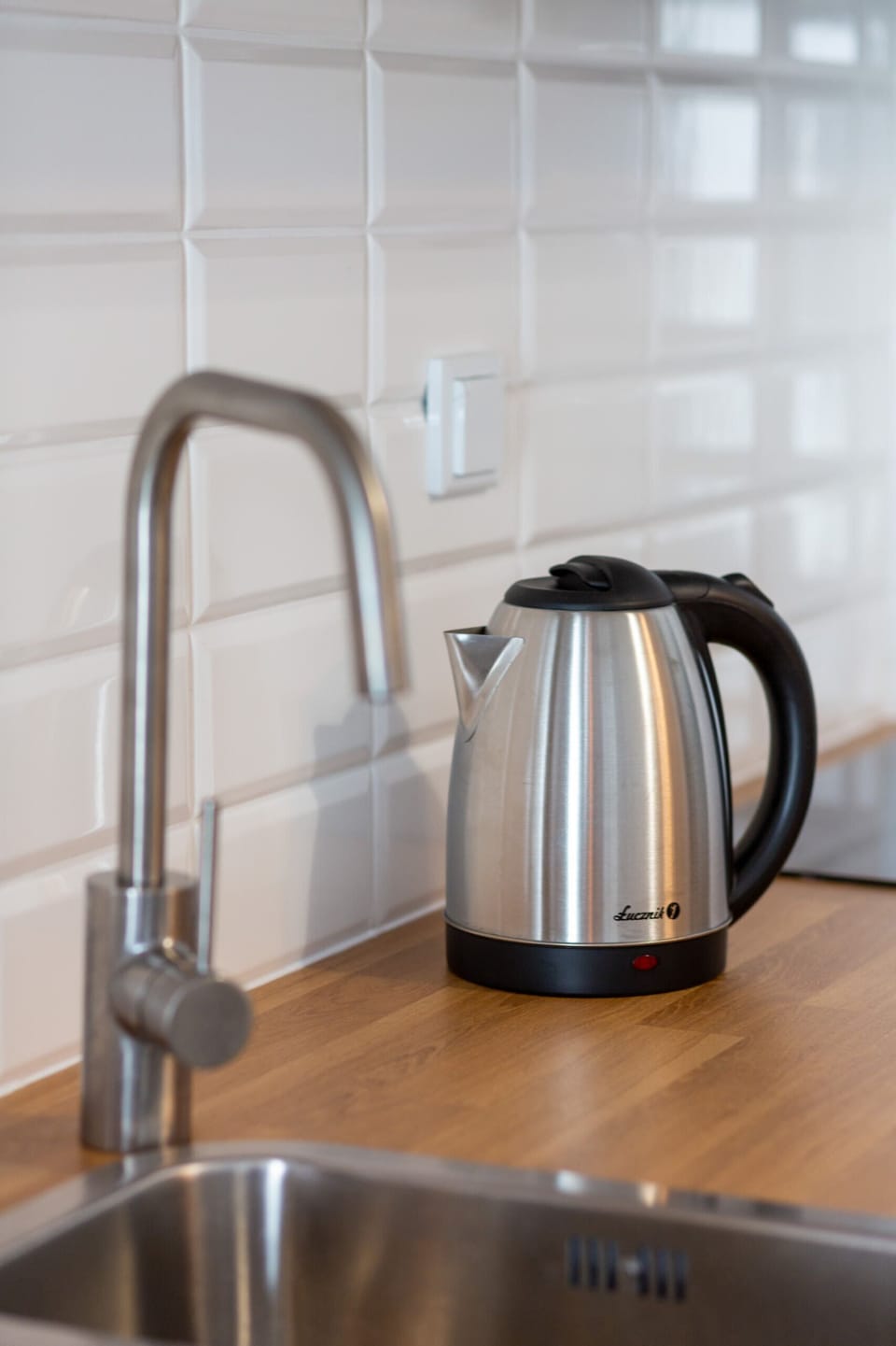 Kitchen corner featuring a sleek sink, kettle, and minimalistic backsplash design.