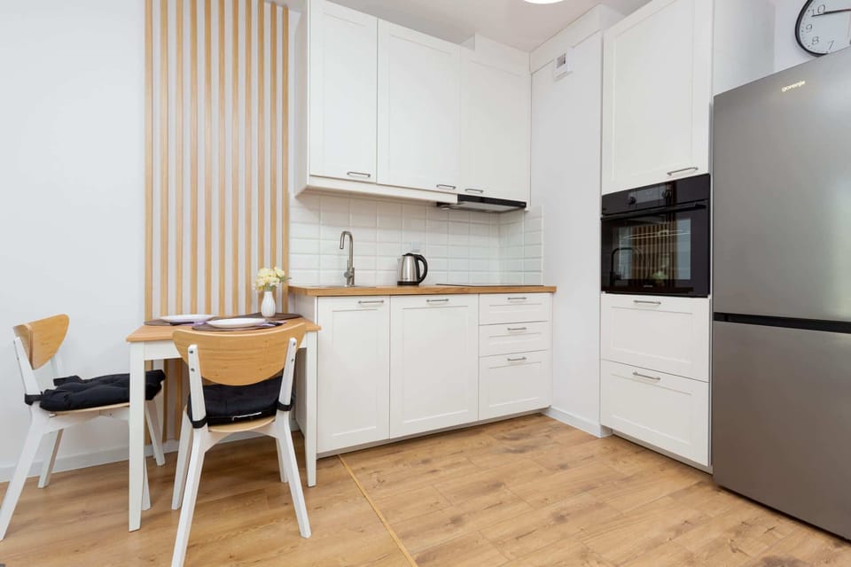 Dining space featuring a wooden table and chairs, adjacent to a fully equipped white kitchen with modern appliances.