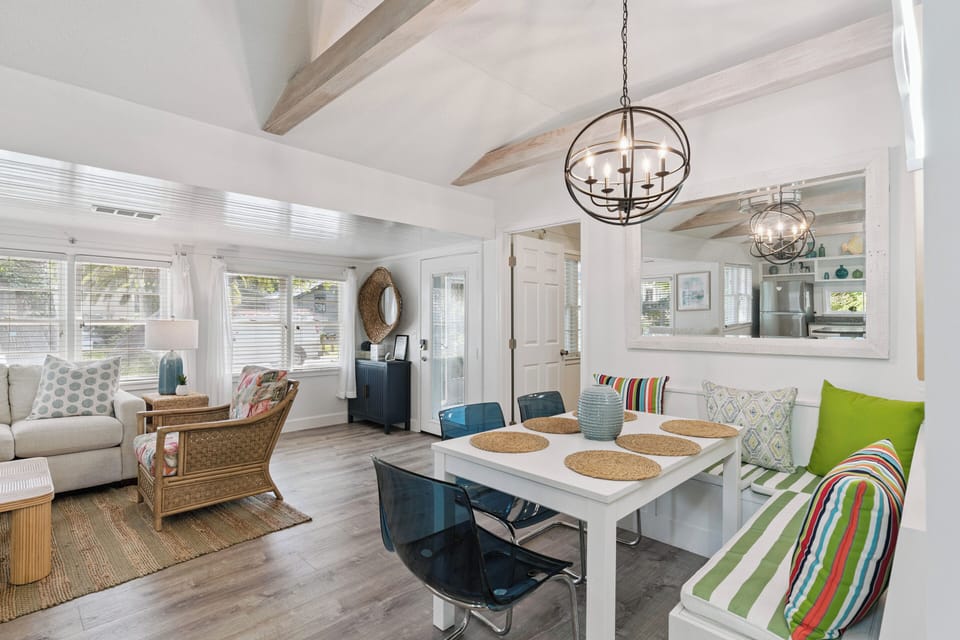 Gather around the table with loved ones in this open, airy dining and living space. Sunlight streams through large windows, wood beam ceilings add warmth, and cheerful pops of color make every meal feel like a celebration.