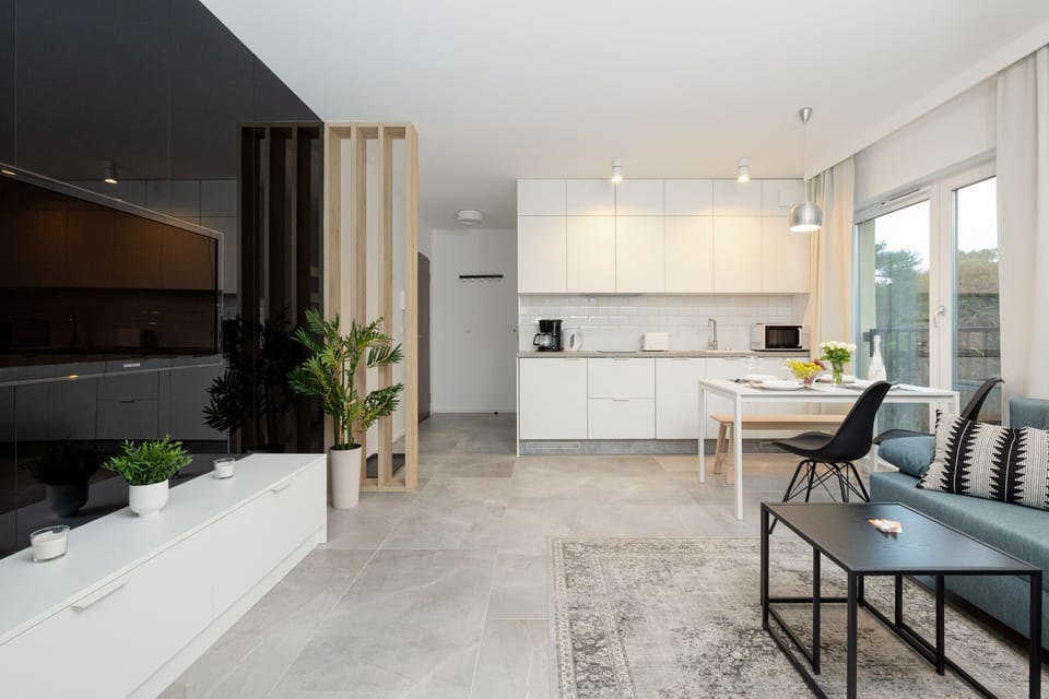  A comfortable living room featuring a TV and a stylish kitchenette in the background. This open layout is perfect for unwinding while keeping the kitchen easily accessible.