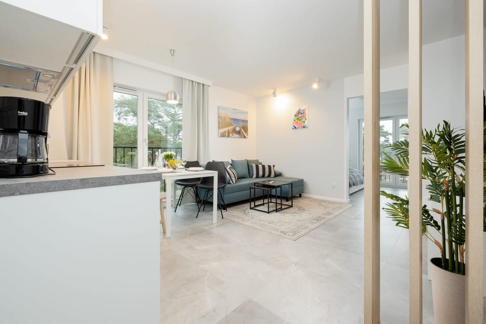 Spacious open area with a dining table and chairs, leading into a living room with comfortable seating by a large window.